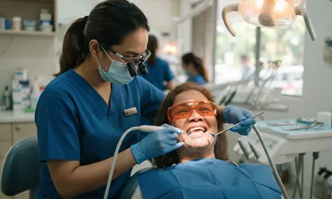 Dental nurse cleaning a smiling patient's teeth while she wears protective glasses